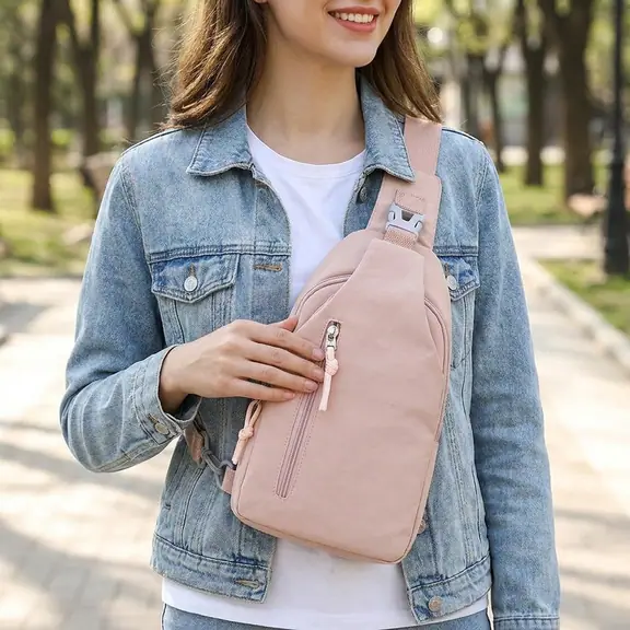 Woman in a denim jacket wearing the pink sling bag across her chest in a park